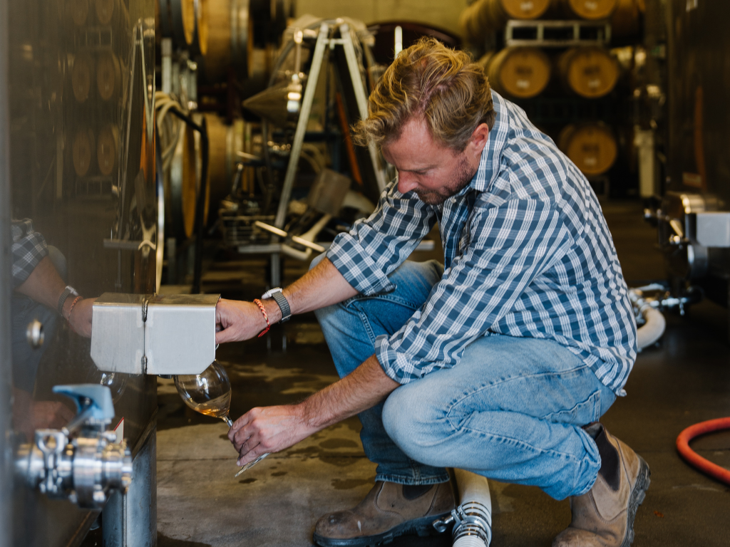 man sampling wine during production from a tank